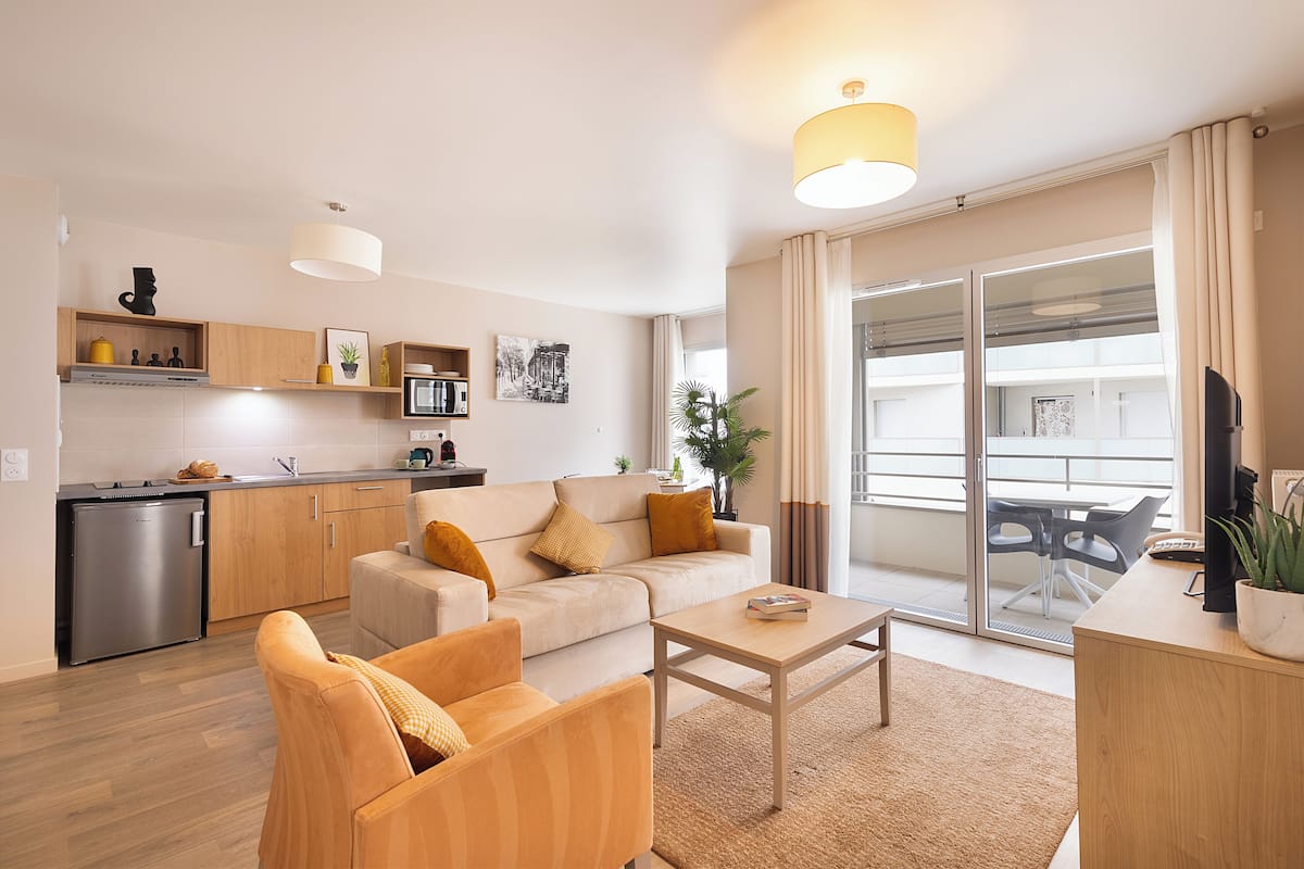 A modern apartment with a kitchenette, a sofa, a coffee table, and a balcony with a view.