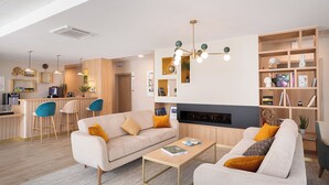 A modern living room with a sofa, coffee table, and a fireplace. There is a kitchen area with bar stools and a counter. - Zenao Appart'hôtels Montreuil (Montreuil)