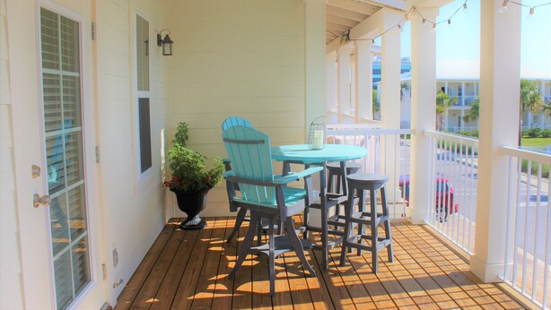 Une terrasse en bois avec une table et des chaises, un pot de fleurs et une vue sur la rue.
