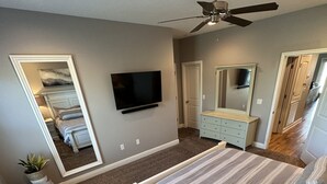 Une chambre à coucher avec un lit, une commode, un téléviseur et un ventilateur de plafond.