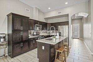 A modern kitchen with dark wood cabinets, stainless steel appliances, and a central island with stools. - El Paso House|SleepNumber&Tempurpedic Beds|85" TV (El Paso)
