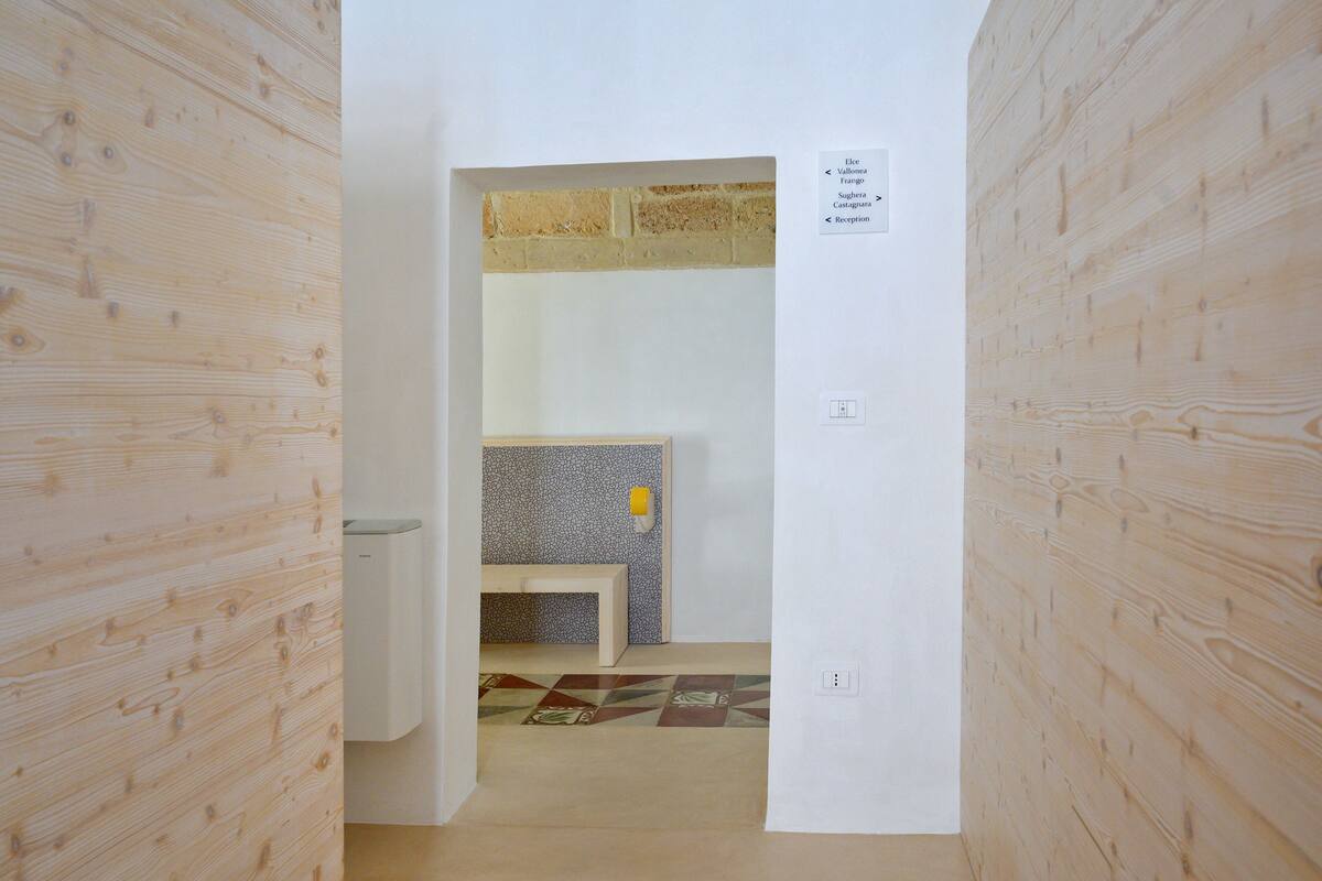 A hallway with wooden walls, a bench, a tiled wall, and a sign indicating room names.