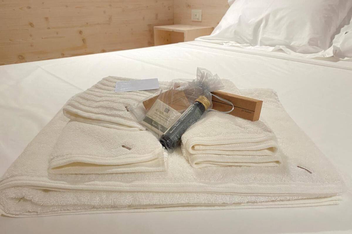 A neatly made bed with folded towels, a bottle, and a small card on a white bedspread in a room with wooden walls.