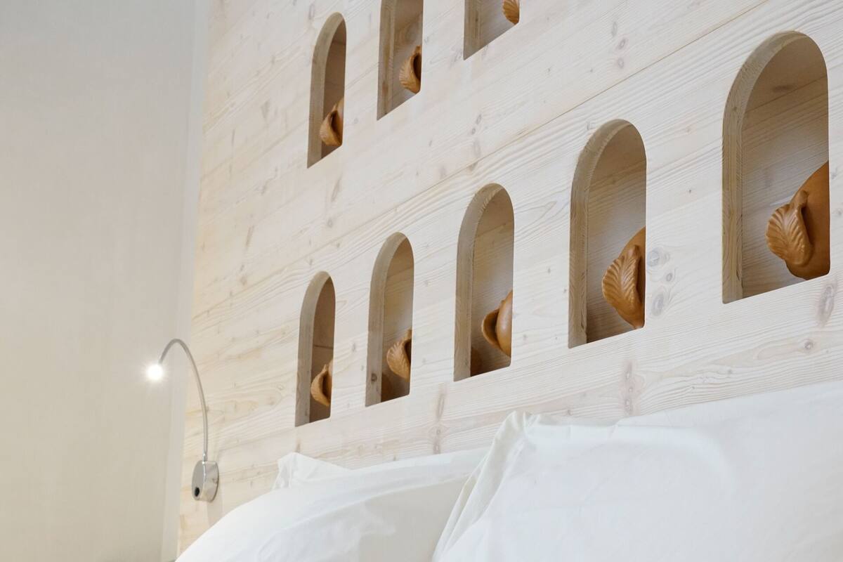 A bedroom with a wooden headboard featuring arched cutouts, a bed with white linens, and a bedside lamp.