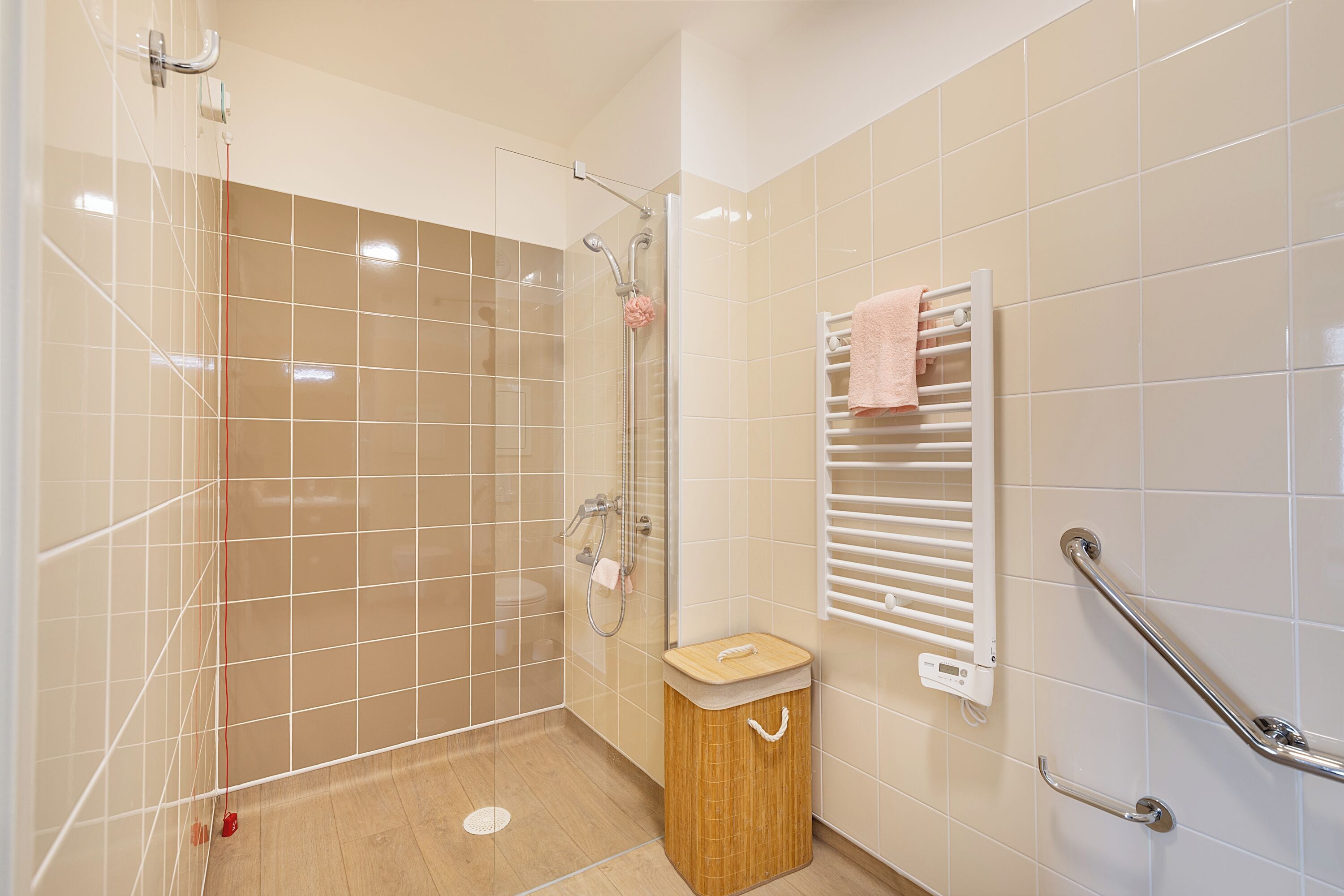 A bathroom with a shower, a toilet, and a sink. There is a towel rack with a pink towel.