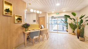 A reception area with a wooden desk, two chairs, a potted plant, and a large mirror. - Zenao Appart’hôtels Le Raincy (Le Raincy)