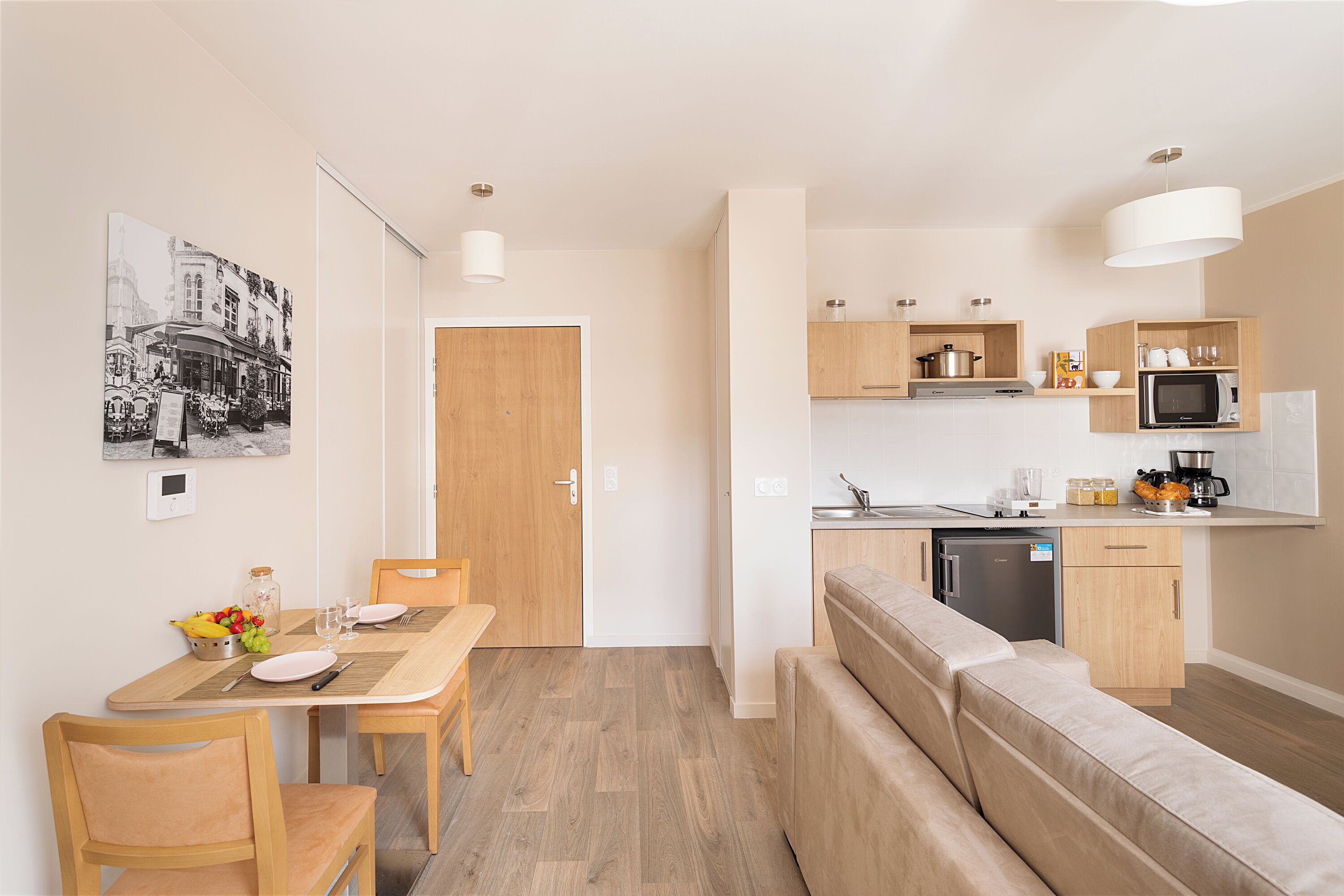 Eine moderne Küche mit Holzausstattung, einer Mikrowelle und einer Kaffeemaschine. Es gibt einen Essbereich mit einem Holztisch und Stühlen sowie ein Sofa im Wohnbereich.