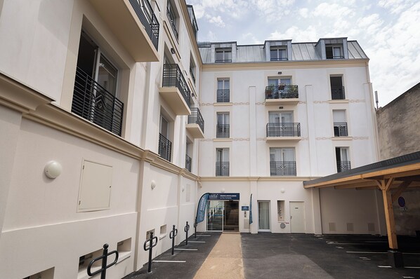 A multi-story building with a central entrance, balconies, and a parking area. - Zenao Appart’hôtels Le Raincy (Le Raincy)