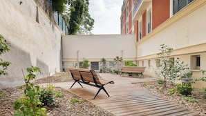 An outdoor courtyard with wooden benches, a paved walkway, and small plants. - Zenao Appart’hôtels Le Raincy (Le Raincy)