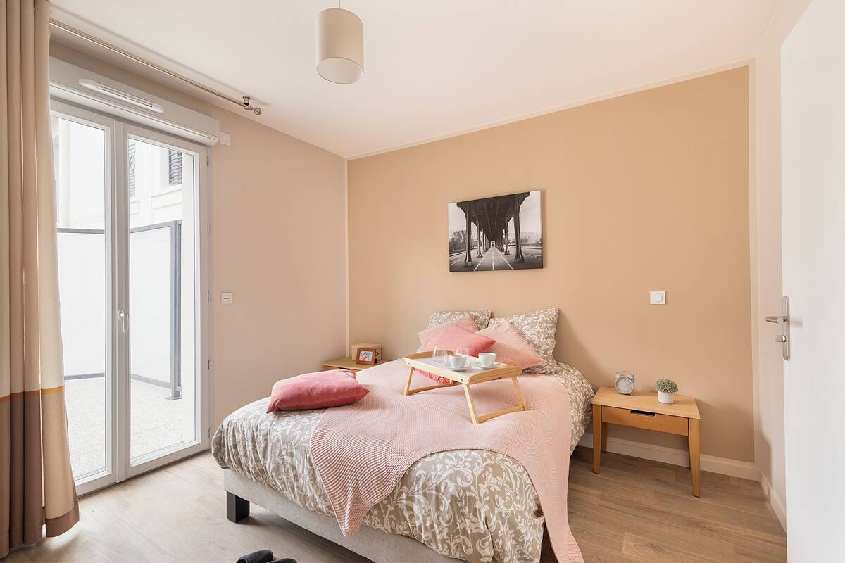 Um quarto com uma cama, mesa de cabeceira, janela e porta.