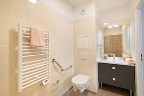A bathroom with a white toilet, a towel rack with a towel, a vanity with a mirror, and a shower area. - Zenao Appart’hôtels Le Raincy (Le Raincy)
