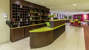 Zona de recepción con mostrador de madera, estantes con plantas en macetas y un área de descanso con sillas.