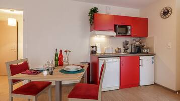 A compact kitchen with red cabinets, a microwave, and a dishwasher. There is a dining table with chairs and a small plant on the counter.