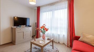 A modern living room with a flat-screen TV, a wooden coffee table, a red sofa, and a large window with sheer curtains.