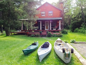 A red house with a porch and three kayaks on the grass in front.