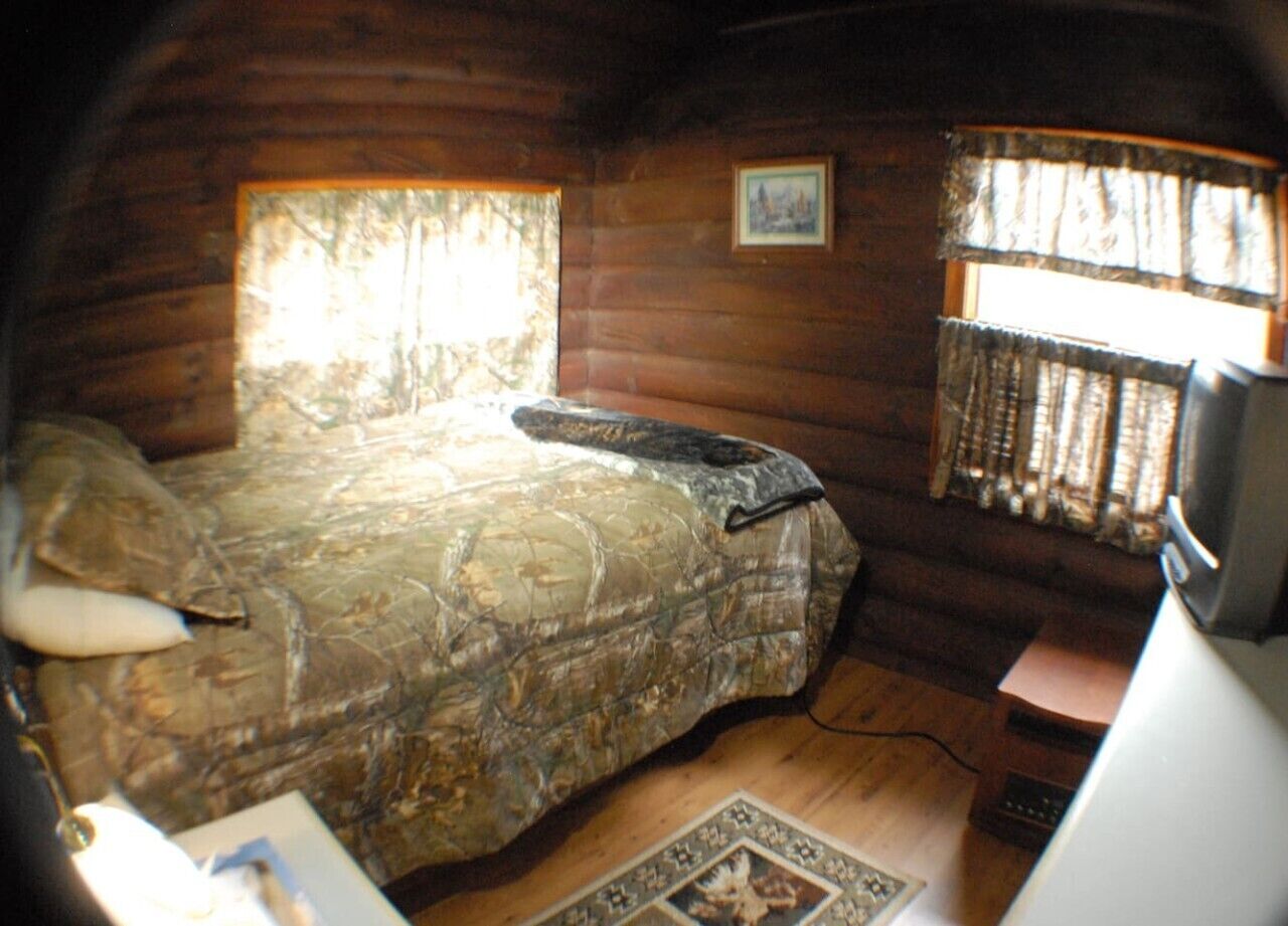 Una habitación con cama, una mesita, una silla, un ventanal con cortinas y un cuadro en la pared.