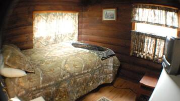 Una habitación con cama, una mesita, una silla, un ventanal con cortinas y un cuadro en la pared.