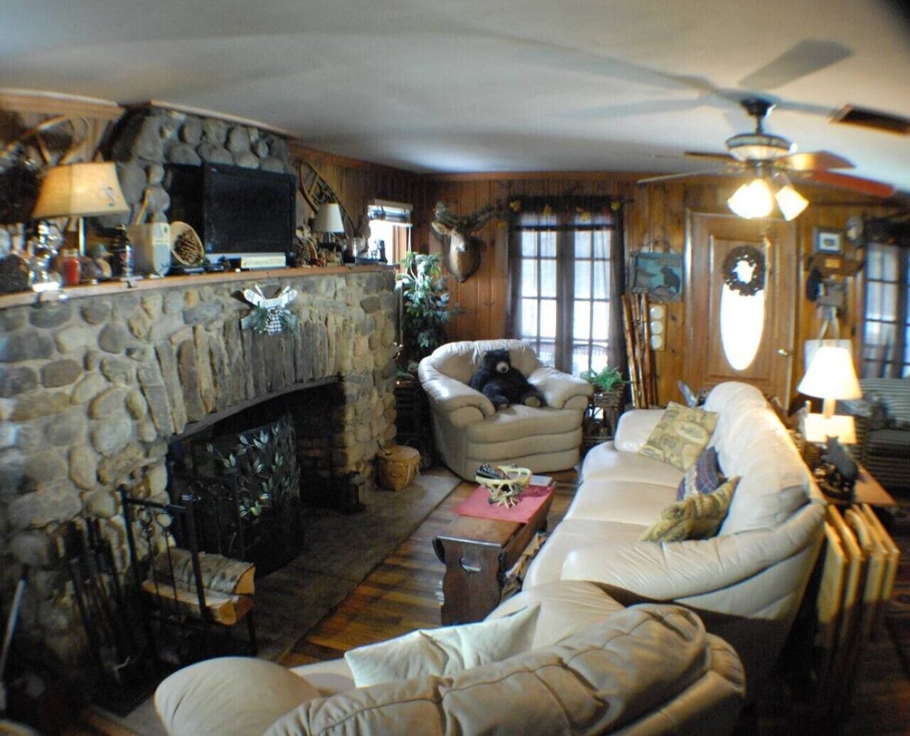A cozy living room with a stone fireplace, a sofa, a chair, and a ceiling fan.