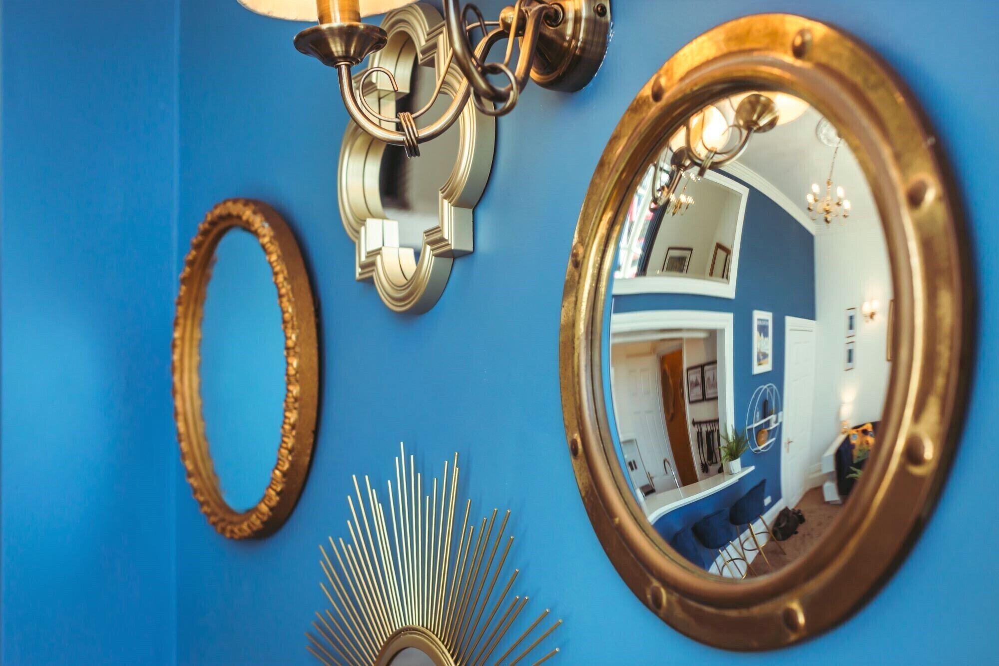 Une pièce avec un mur bleu, un miroir reflétant une partie de la cuisine et un miroir décoratif en forme de soleil.