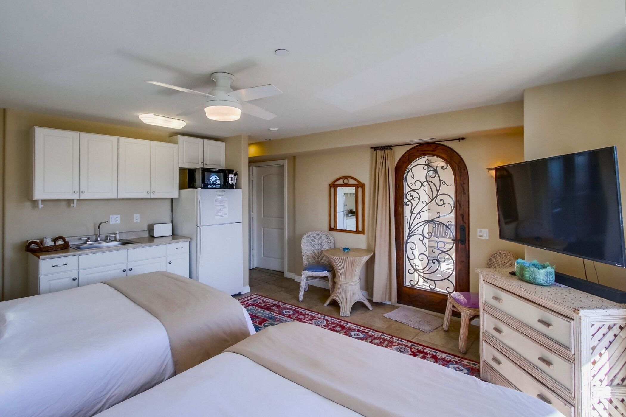 Habitación de hotel con kitchenette, dos camas, un televisor, un espejo y una puerta decorativa.