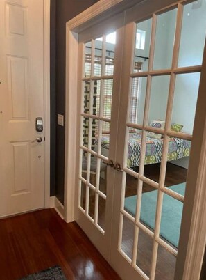 A room with a wooden floor, a white door, and a glass door leading to a bed with a patterned bedspread. - Cheerful 4 Bed, 3 Bath Home with Screened Pool (Winter Haven)