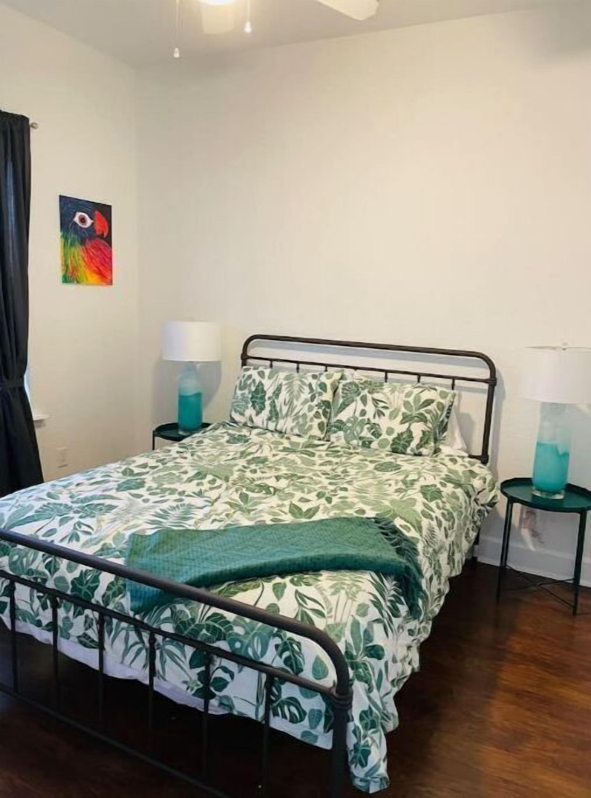 A bedroom with a bed, two bedside tables, a nightstand, a lamp, and a painting on the wall.