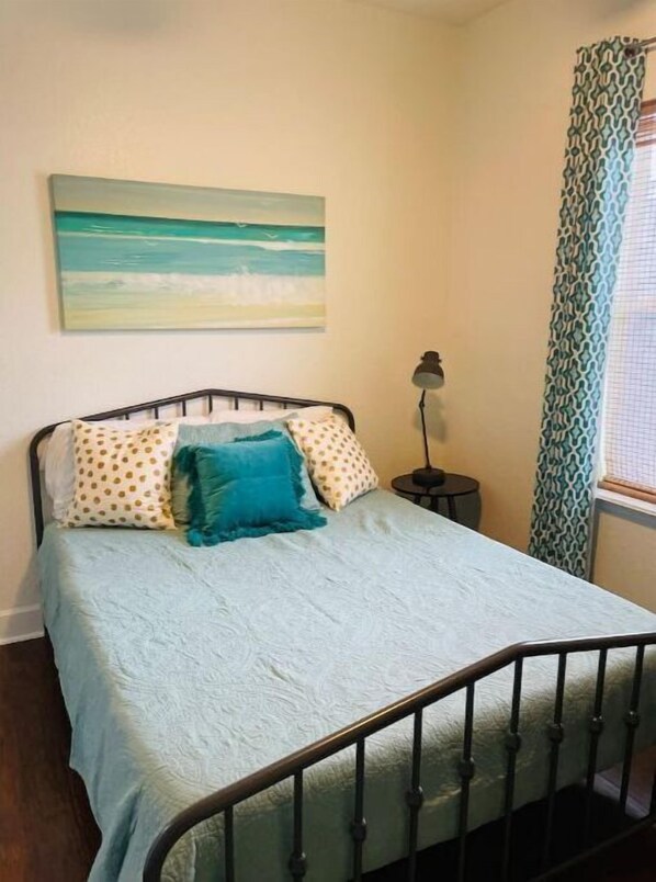 A bedroom with a bed, a nightstand, a lamp, and a painting of a beach scene.