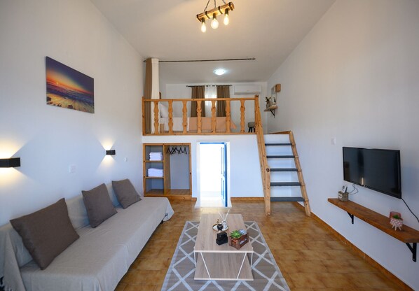 Ein geräumiger Wohnbereich mit Sofa, Couchtisch, Fernseher und einer Treppe, die in eine obere Ebene führt.
