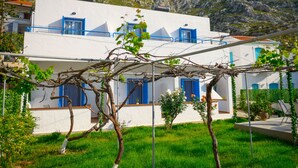 Een wit gebouw met blauwe luiken en een pergola begroeid met wijnranken op de voorgrond.