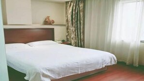 Une chambre d’hôtel avec un grand lit, une tête de lit en bois, une table de chevet, un objet décoratif sur le mur et une fenêtre avec des rideaux.