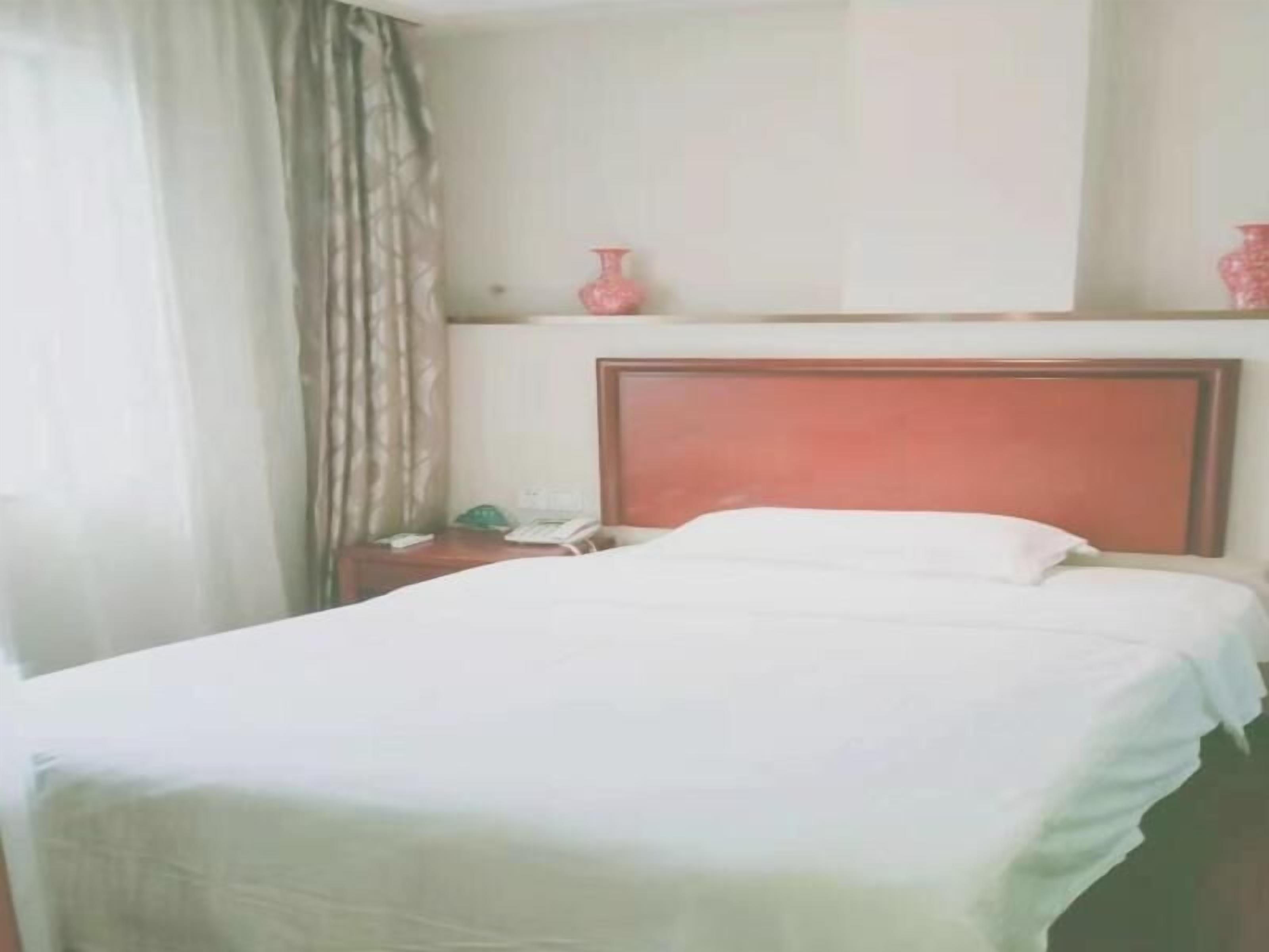 A hotel room with a bed, a nightstand, a telephone, and a vase on the wall.