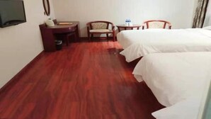 Une chambre d’hôtel avec un plancher en bois, un bureau avec une chaise, un lit et un téléviseur fixé au mur.
