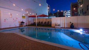 Une piscine intérieure avec un sol carrelé, entourée de chaises longues et de parasols rouges.