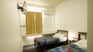 Une chambre d’hôtel avec deux lits simples, une fenêtre avec des rideaux, un appareil de climatisation et une petite table de chevet avec une lampe.
