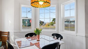 A dining area with a table set for four, two chairs on each side, a vase with flowers, and a colorful stained glass light fixture above. - Relax and unwind in a tranquil space one block from the beach (Manzanita)