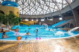 Ein Hallenbad mit mehreren Bahnen, einer Rutsche und einem Spielbereich.