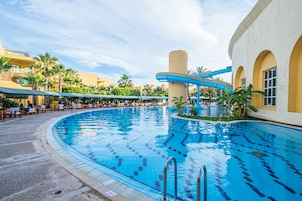 A large indoor swimming pool with a curved design, surrounded by palm trees and a covered seating area.