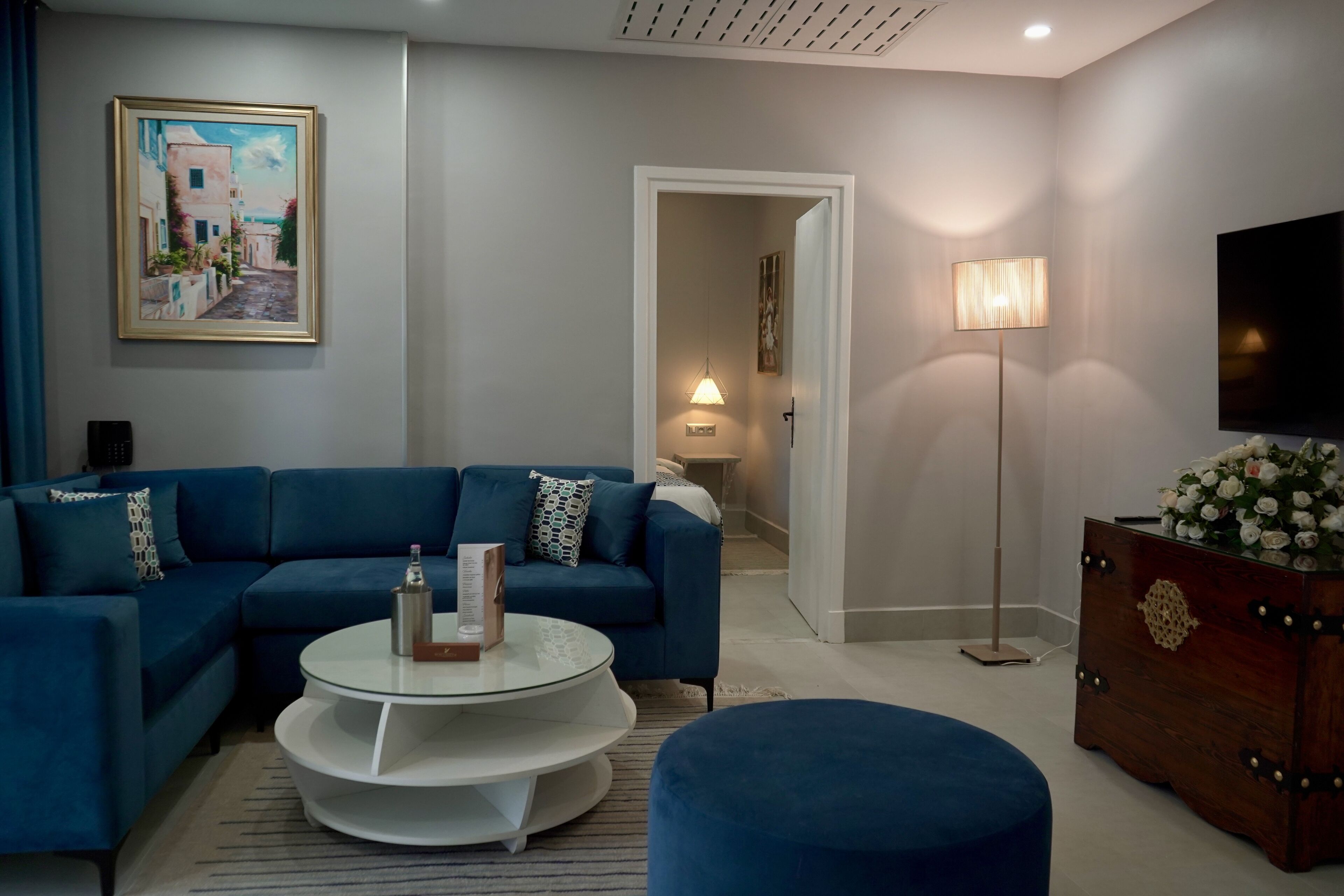 Una sala de estar moderna con un sofá azul, una mesa de centro redonda y un aparador de madera con flores.