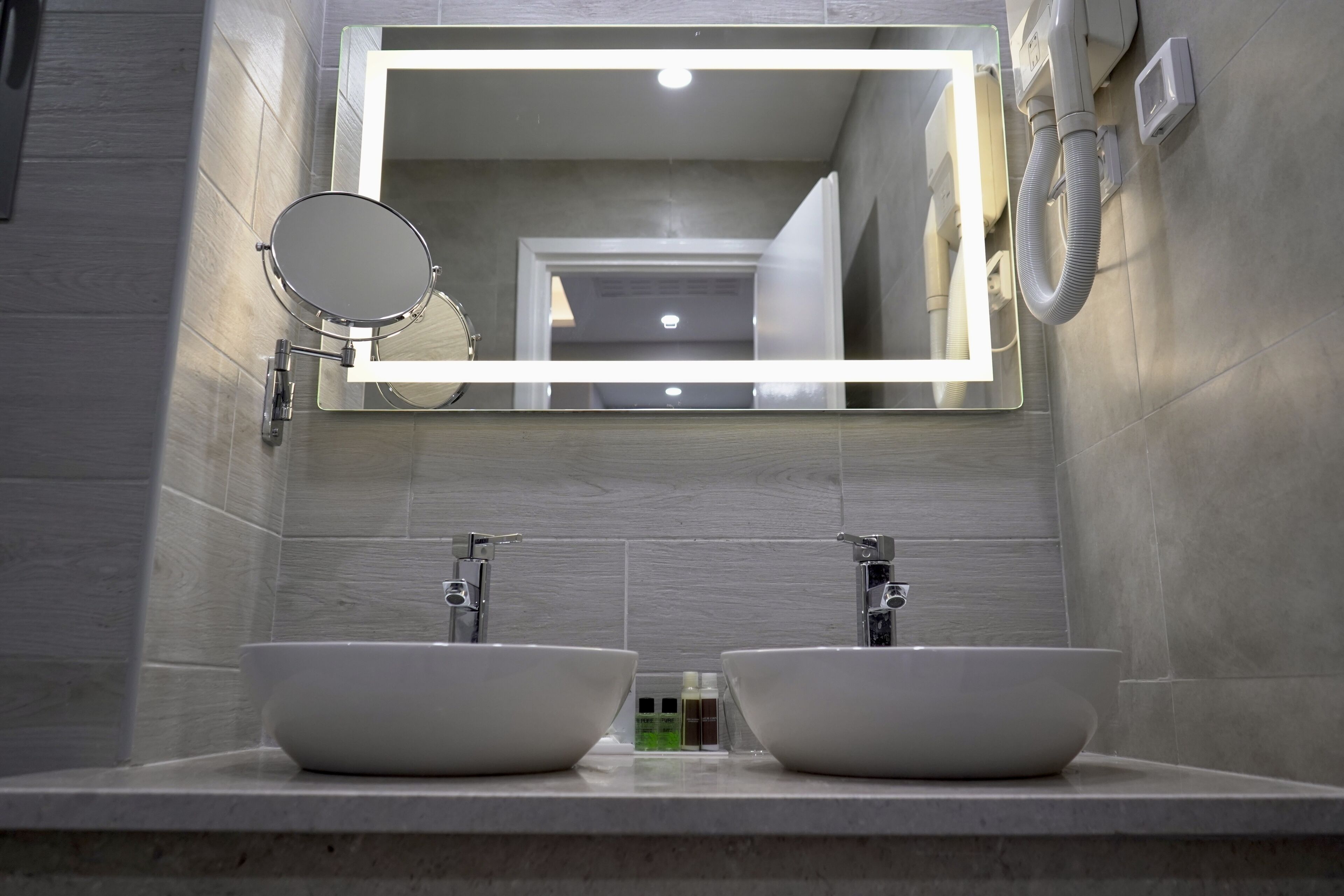 A bathroom with two sinks, a mirror, and a lighted mirror frame.