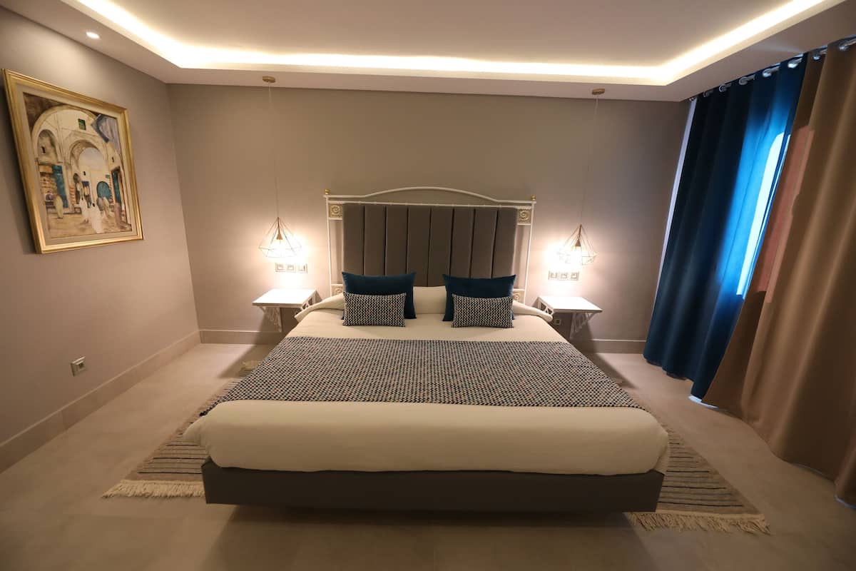 A modern hotel room with a large bed, two bedside tables, a headboard, and a painting on the wall.