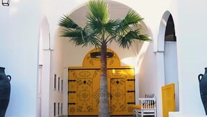 A hallway with a palm tree, a yellow door, and a staircase leading to an upper level. - Suites hotel les charmilles & spa (La Marsa)