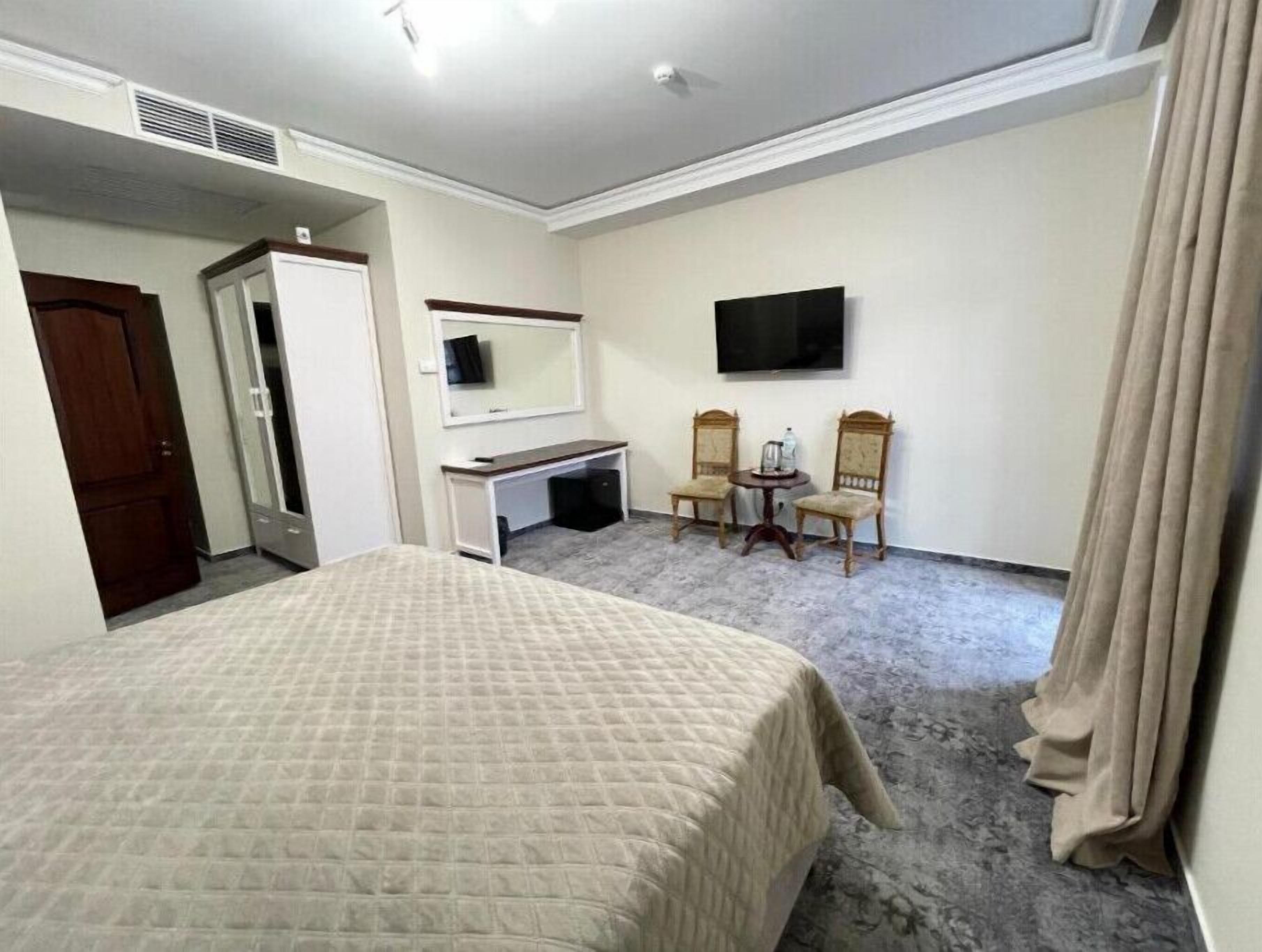 A hotel room with a bed, a desk, two chairs, a TV, and a door.