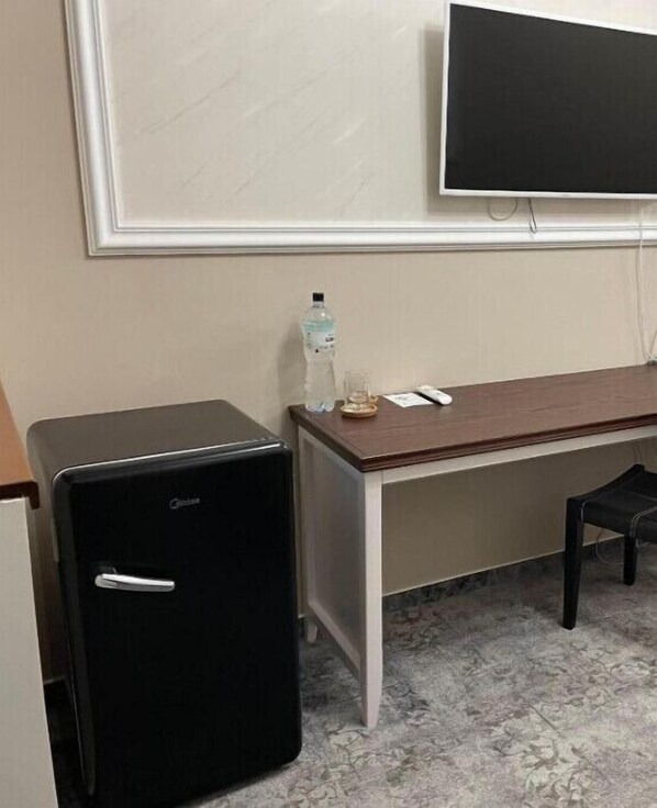 A small black refrigerator, a wooden desk with a chair, a bottle of water, and a television mounted on the wall. - Villa ACAEM #4 (Chișinău)