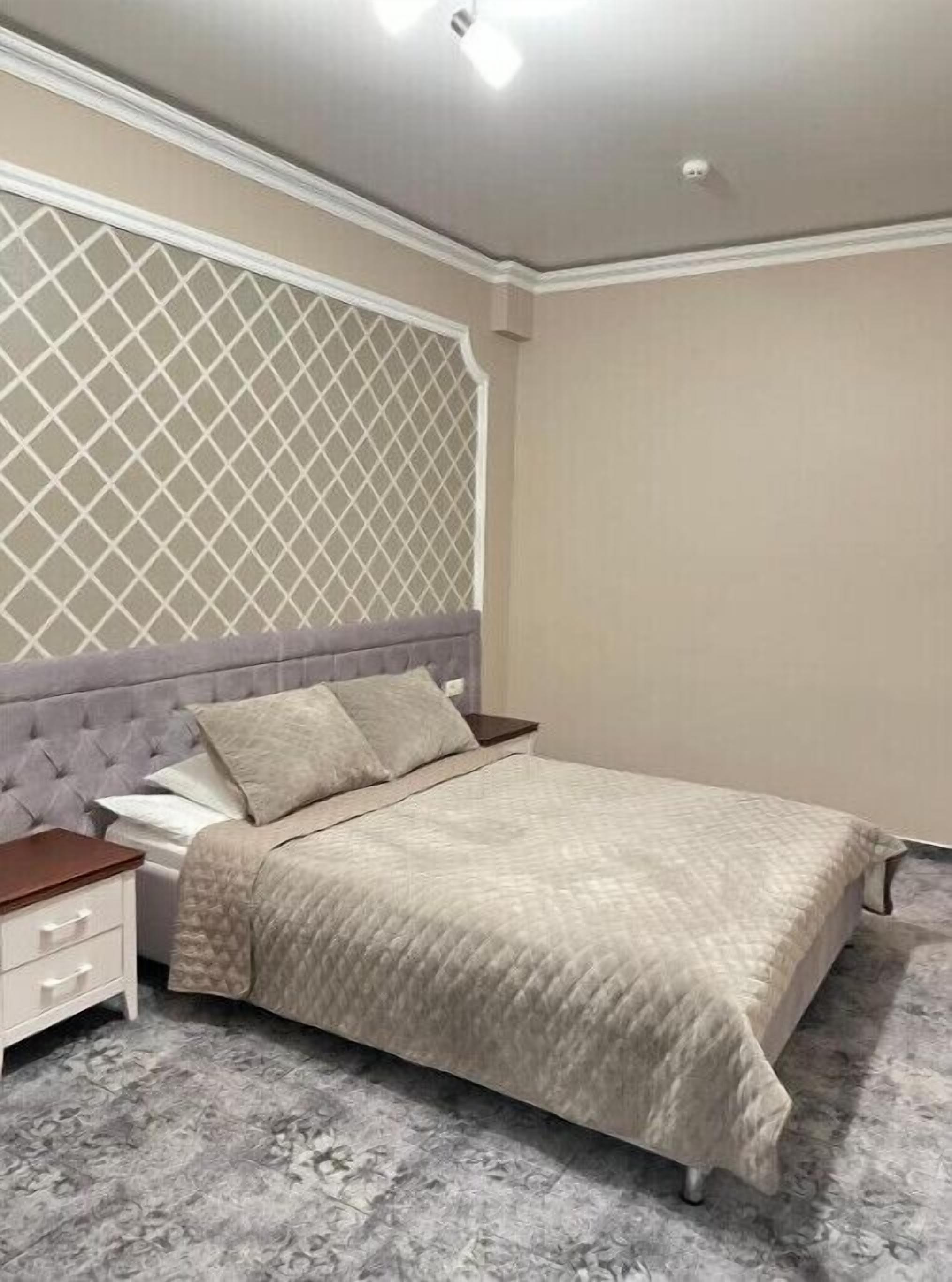 A bedroom with a bed, nightstand, and a decorative wall panel.
