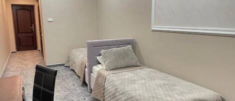 A bedroom with two single beds, a wooden desk, and a chair.