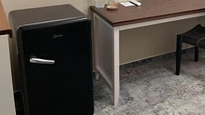 A small black refrigerator, a wooden desk with a chair, a bottle of water, and a television mounted on the wall. - Villa ACAEM #9 (Chișinău)
