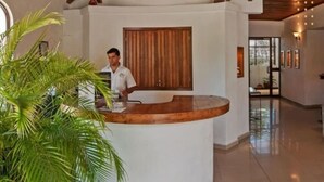 A reception area with a wooden reception desk, a receptionist, and a large potted plant. - Hotel Pez Vela (Manzanillo)