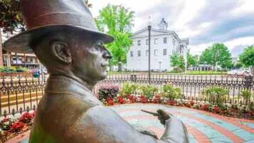 A statue of a man in a hat pointing to a building in the background.