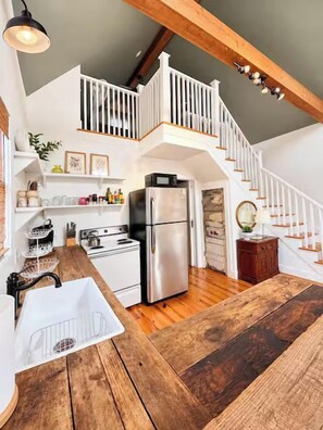 A kitchen with a wooden table, white cabinets, a stainless steel refrigerator, and a white staircase. - The Cottage, Firepit+ Animals, VelvetDitchVillas (Oxford)