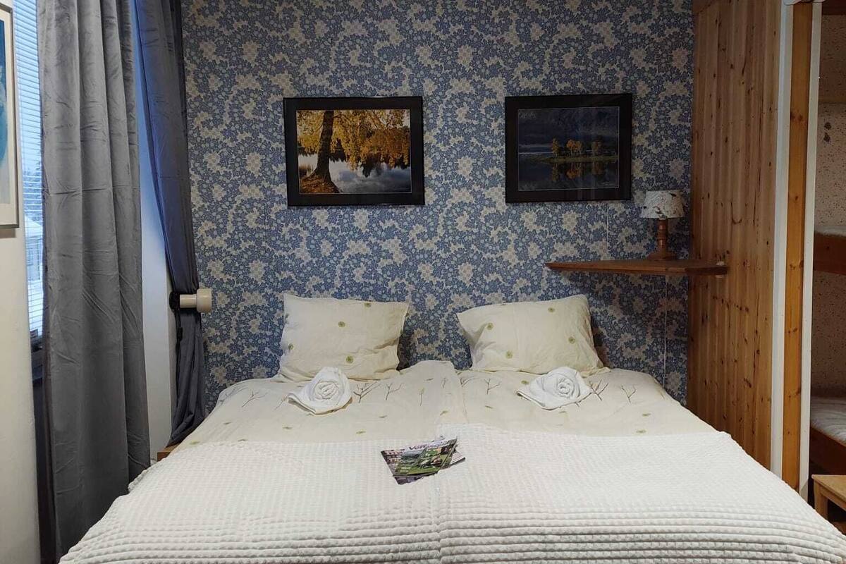 Un dormitorio con una cama grande, dos cuadros enmarcados en la pared, un estante de madera y una ventana con cortinas.